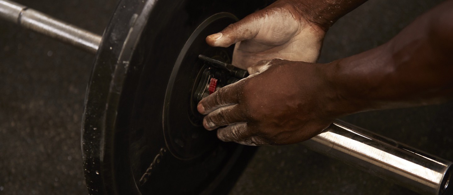 Two hands securing a weight plate onto a barbell, chalk on the fingers.