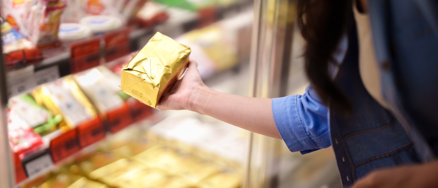 A hand lifting a plain foil-wrapped package from a chilled shelf.