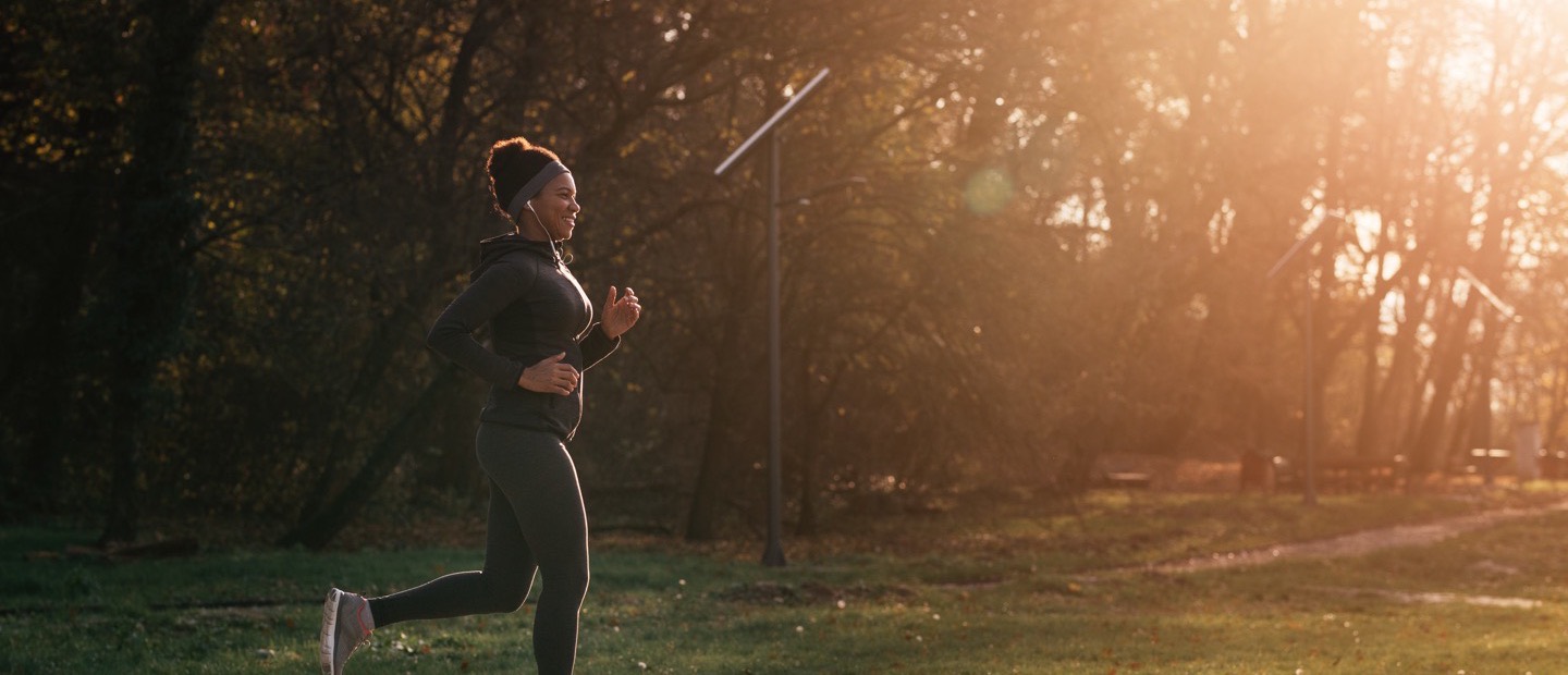 A runner on a park path in low morning sun, seen from the side.