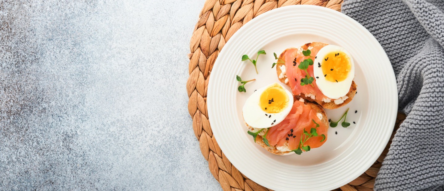 An overhead plate of salmon, boiled egg and microgreens on a woven mat.